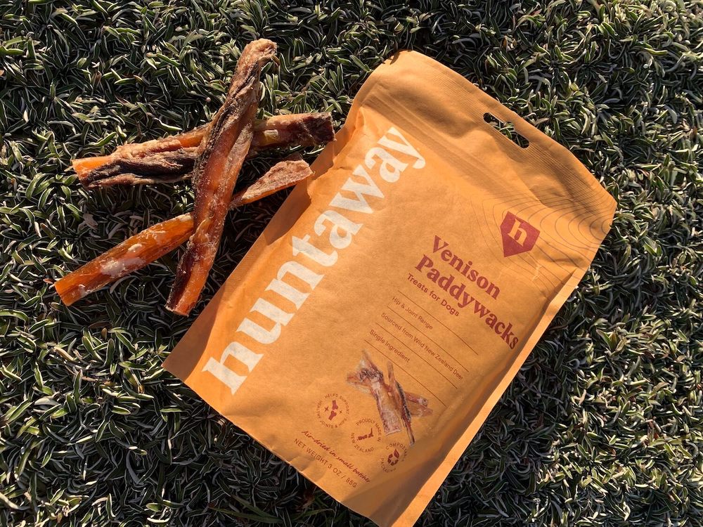A flatlay of 3 Venison Paddywacks treats and the accompanying bag, lying on the grass